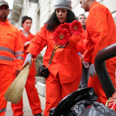 Жена в работно облекло поставя гербери в чувалите с боклук, които стовариха общинските съветници пред сградата на общината