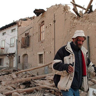 Ранен мъж се разхожда пред срутените постройки в селище край Акуила