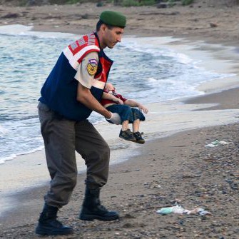 Полицай носи телцето на детето на бежанци, изхвърлено на брега